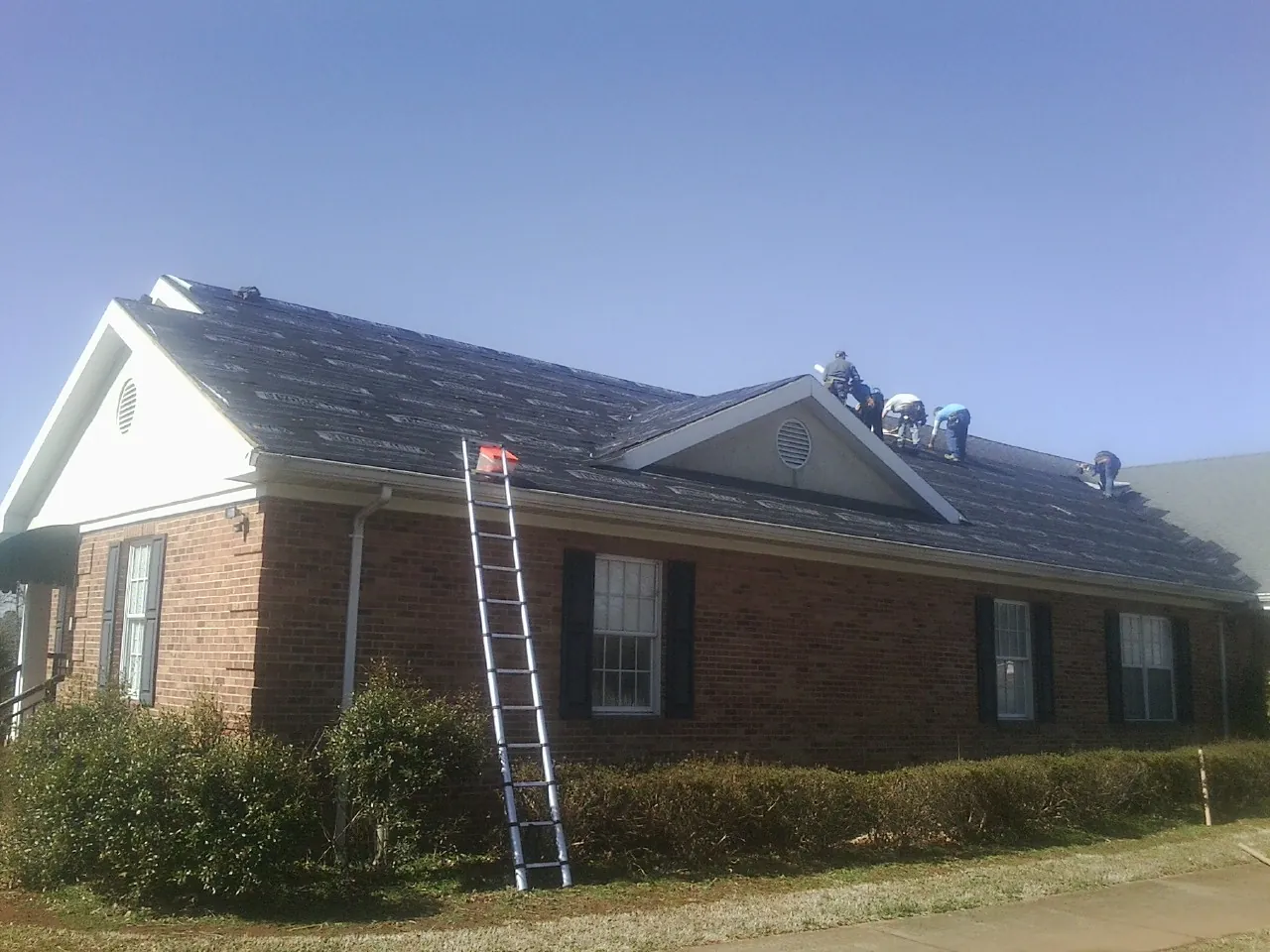 Crew tearing shingles off a brick ranch roof with a ladder set — Emergency Roof Repair work by our crew in Bernville