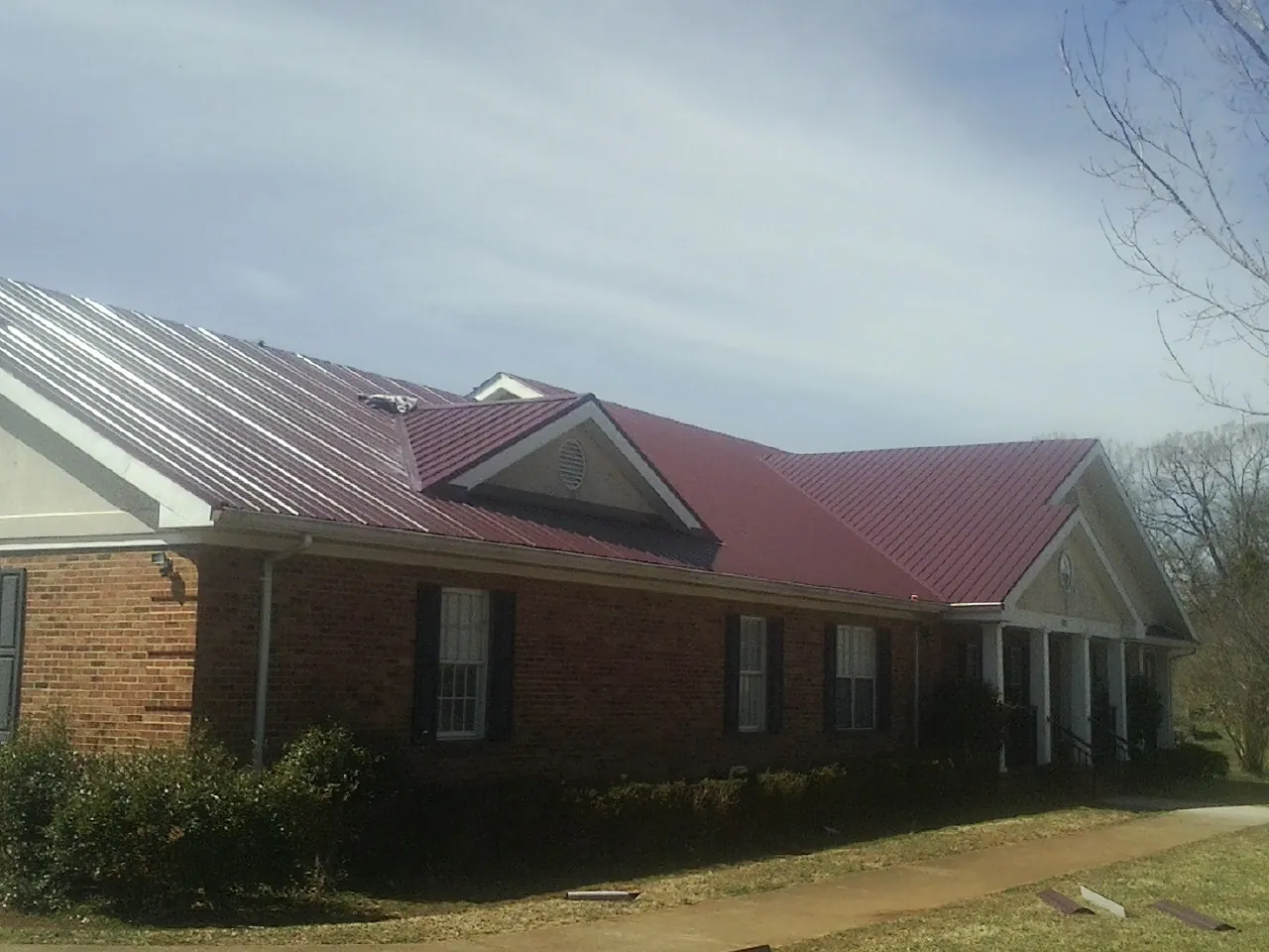 Red metal roof with gabled entries on a long brick building, from a Hail Damage Roof Repair job in Bernville