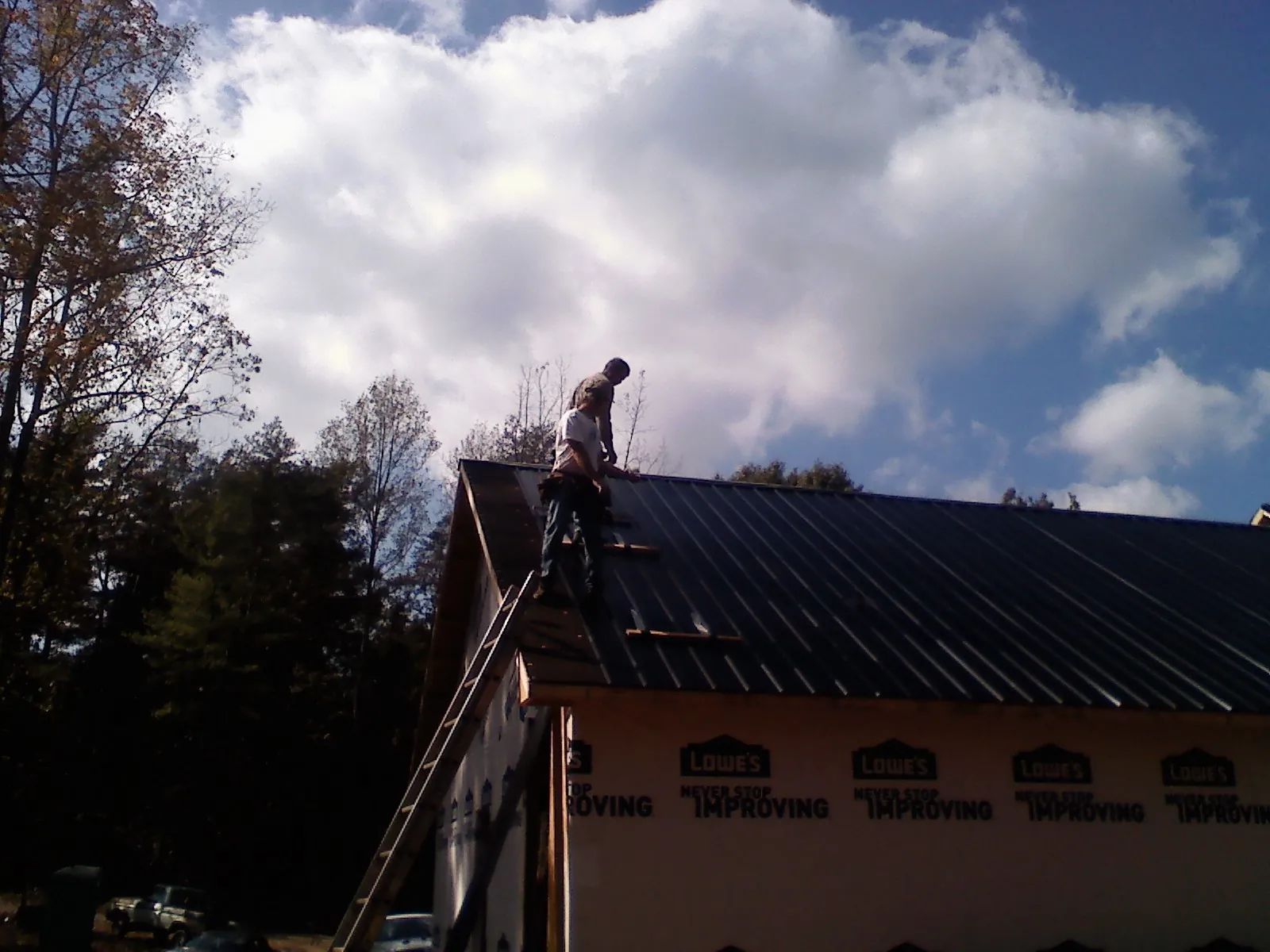 Roofer fastening dark metal panels high against a cloudy sky, from a Roof Inspection job in Bernville