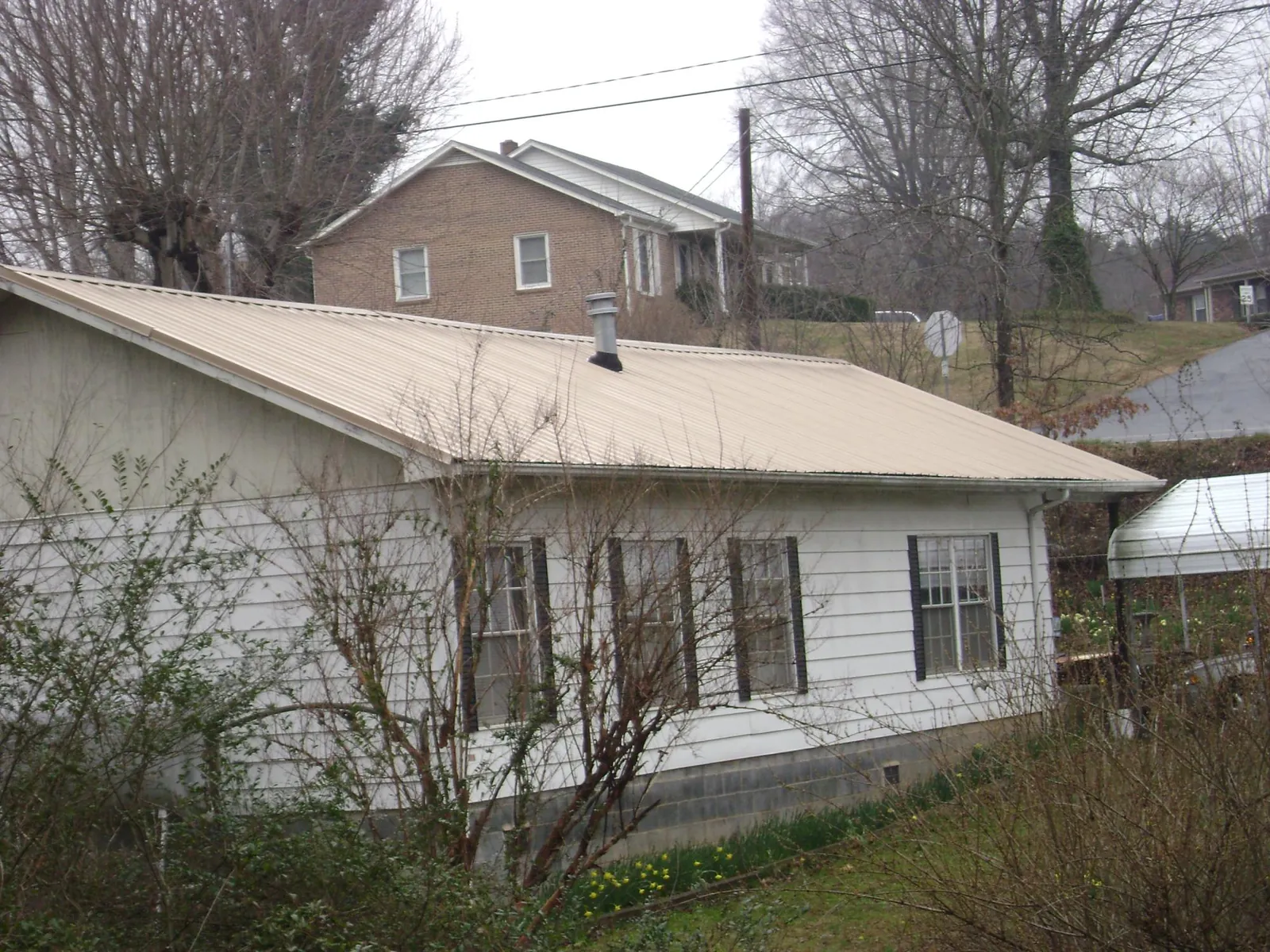Tan metal roof on a white sided house set into a hillside — Commercial Roofing by Roofing Brothers in Bernville
